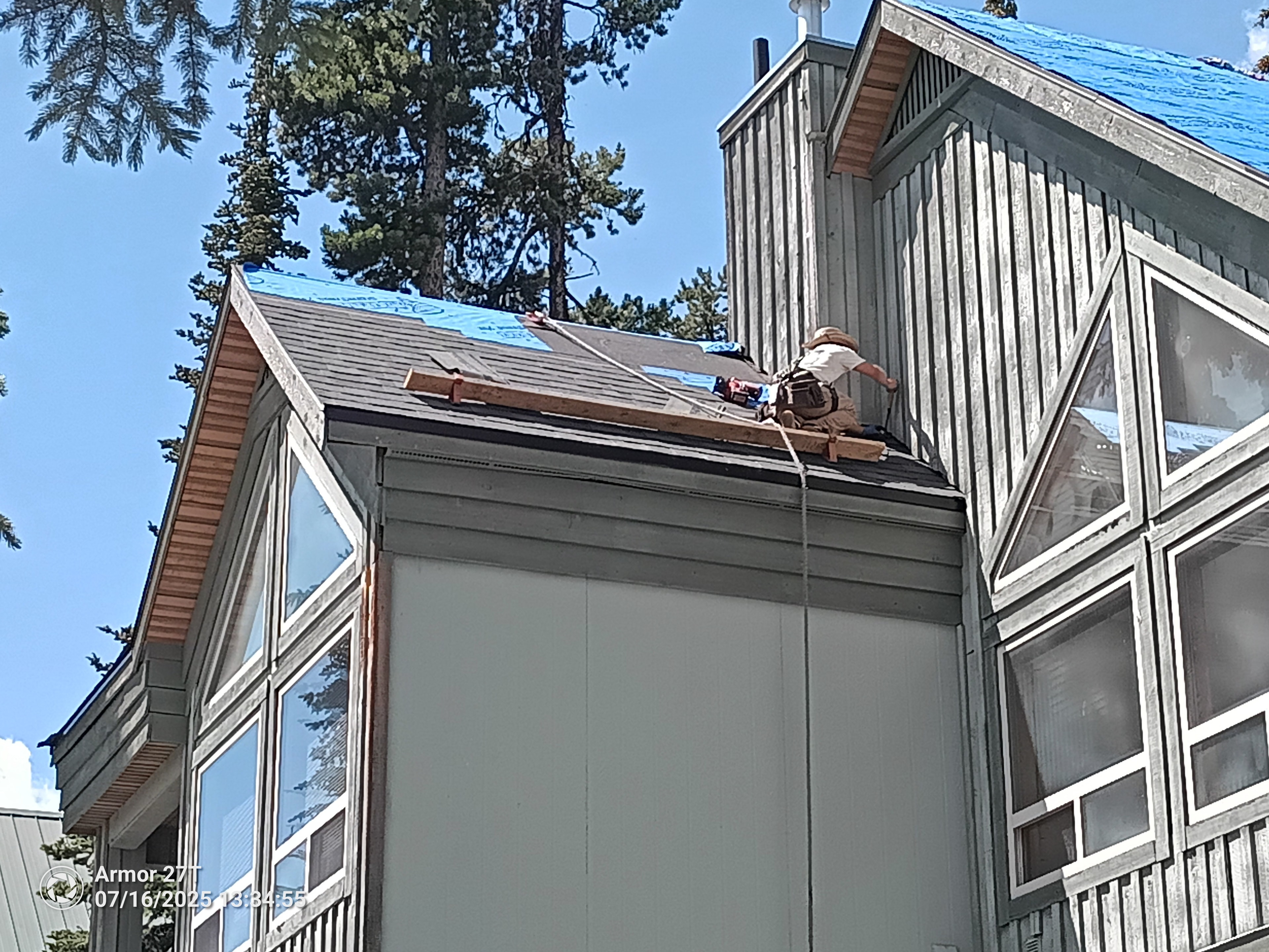 Roofer working on chalet-style home with blue underlayment visible at Big White