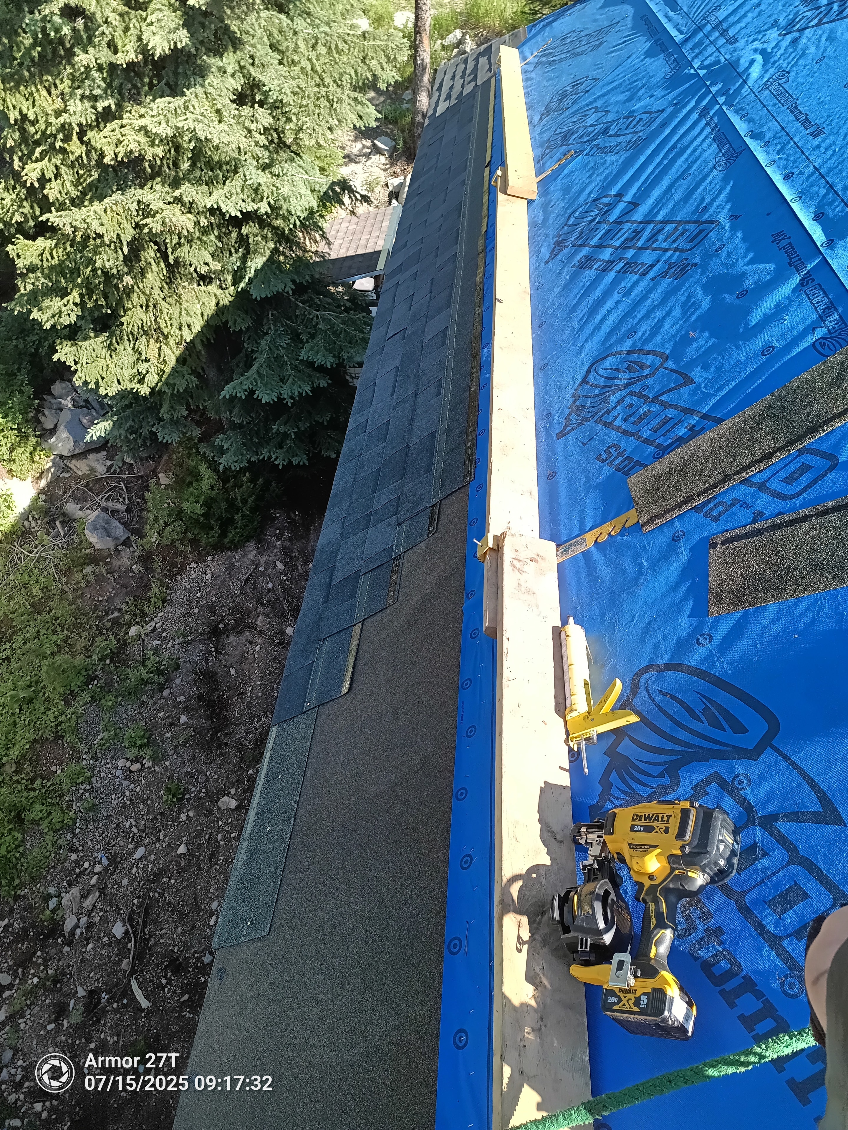 Shingle installation in progress with DeWalt tools on steep roof with blue StormTred membrane