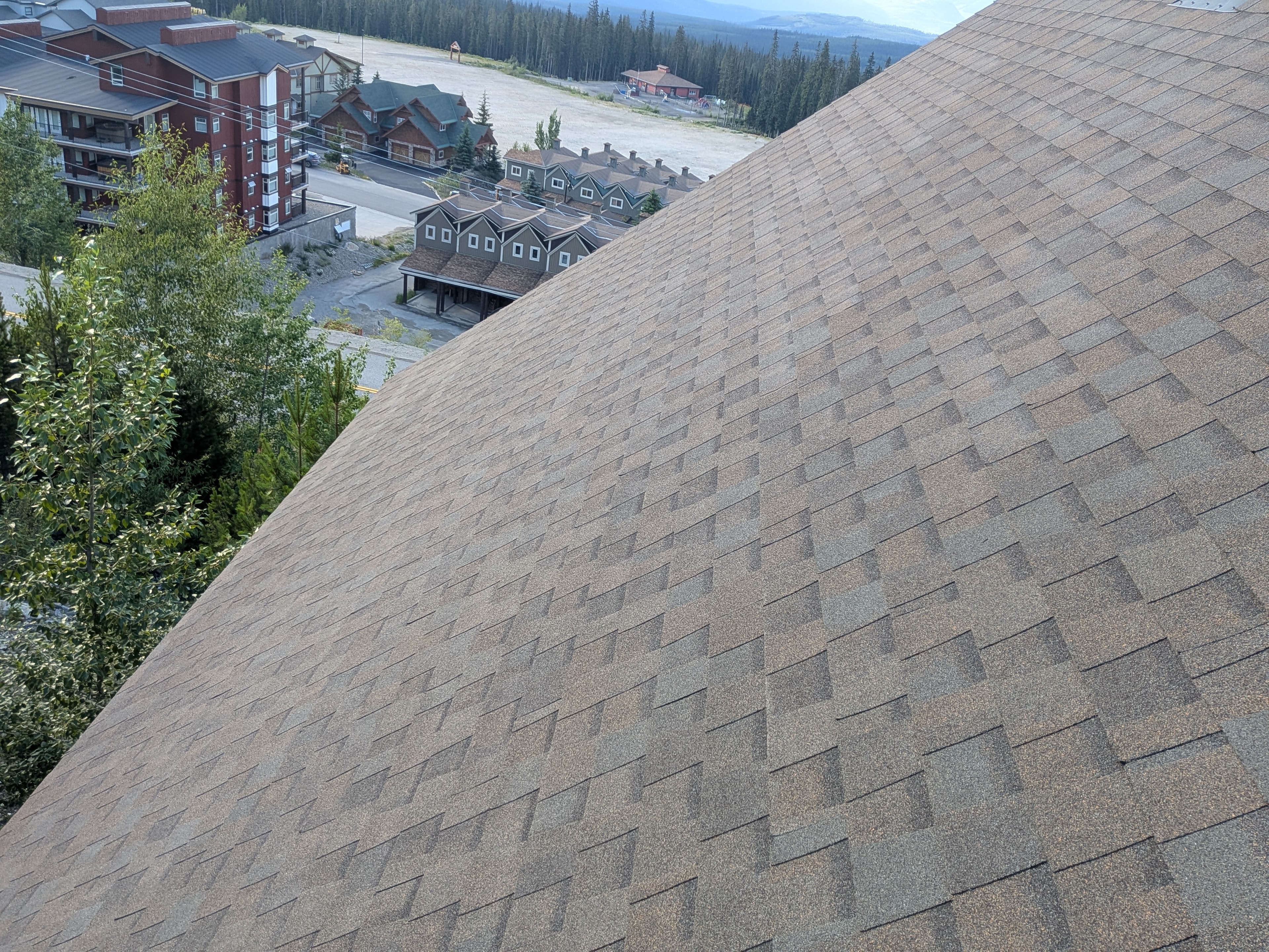 Completed tan/beige shingle roof on large resort building at Big White with mountain views