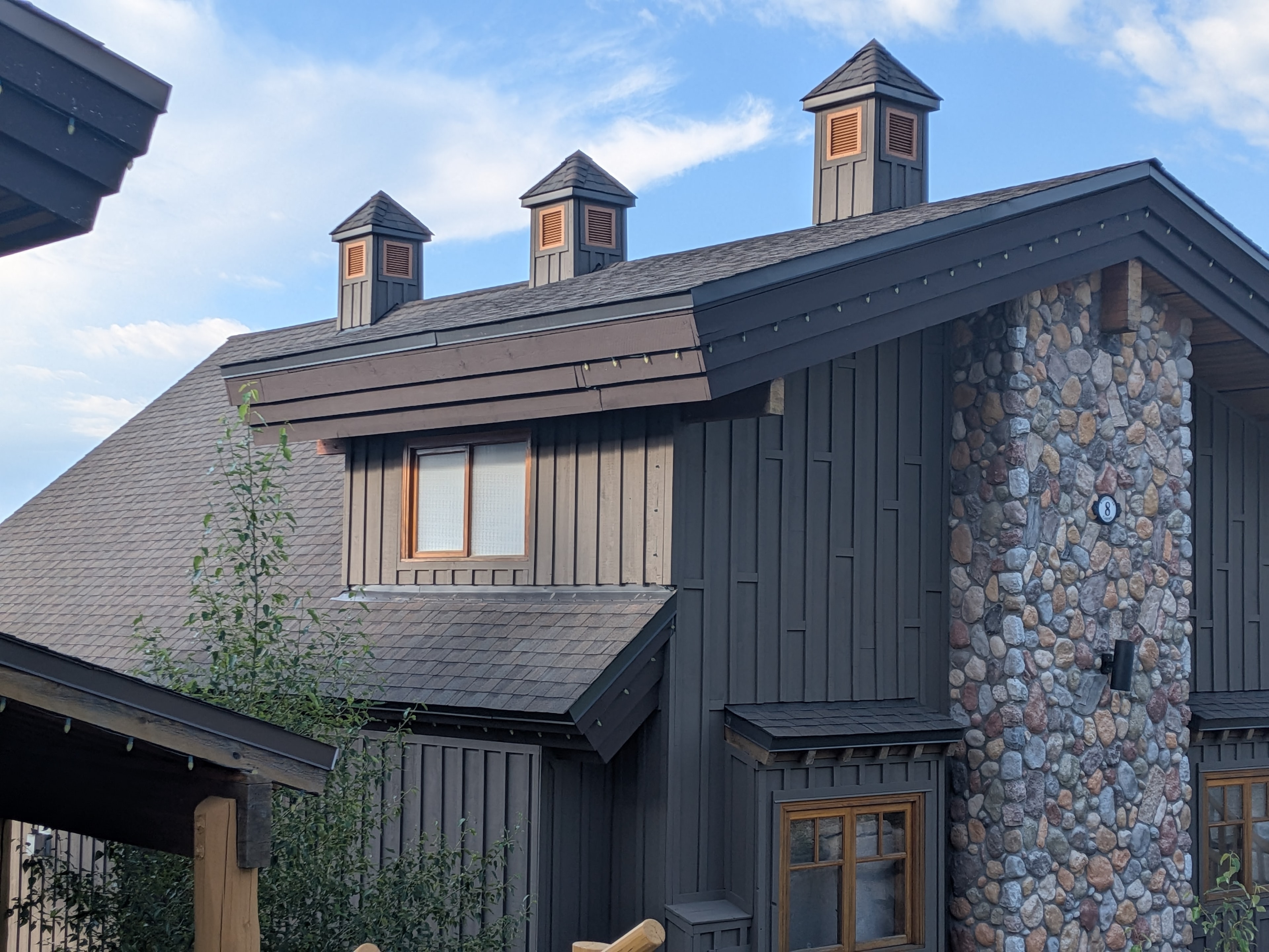 Dark shingle roof with multiple cupolas on chalet-style building with stone accents at Big White