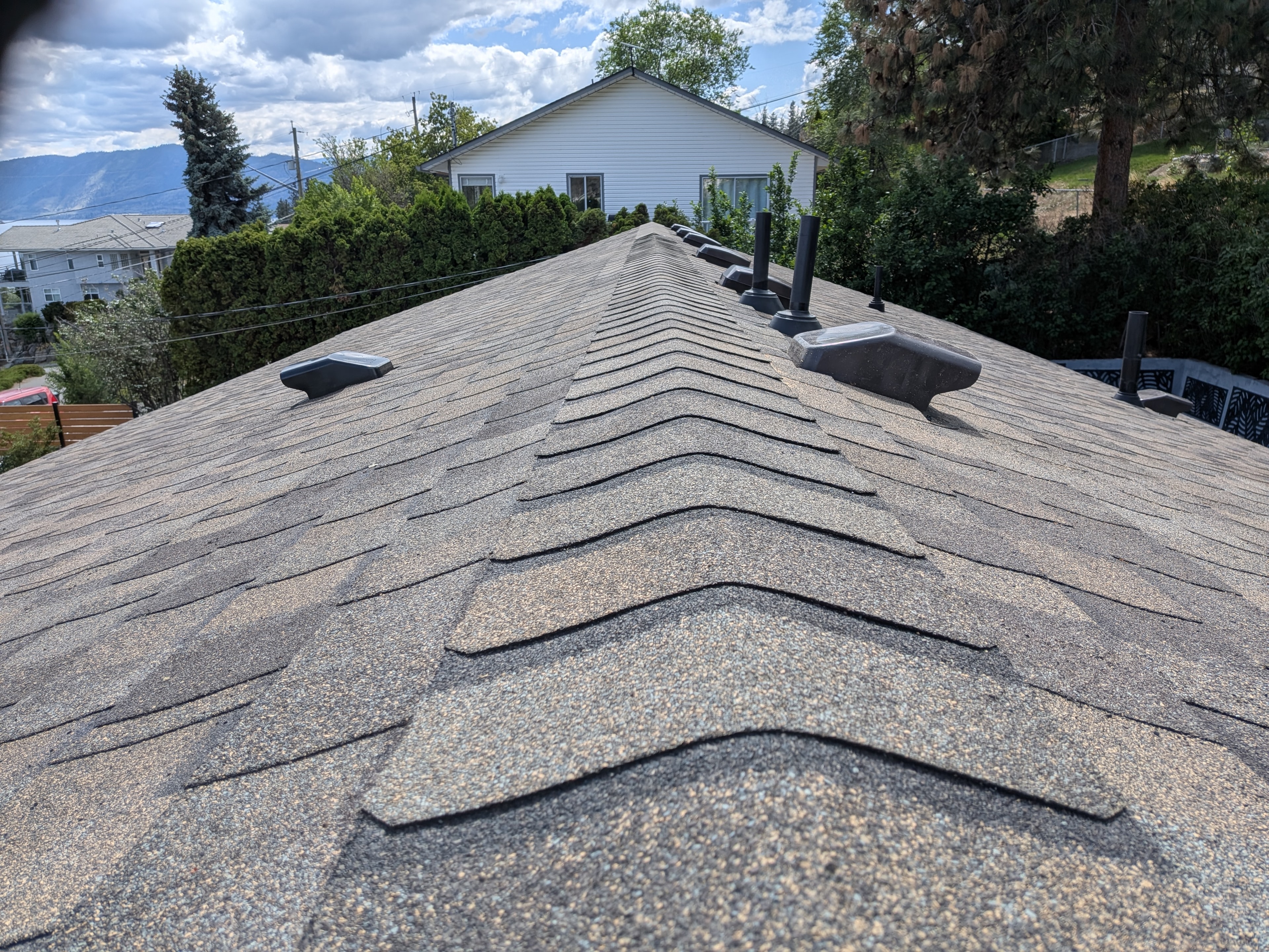 Completed shingle roof ridge with roof vents and Kelowna neighbourhood backdrop