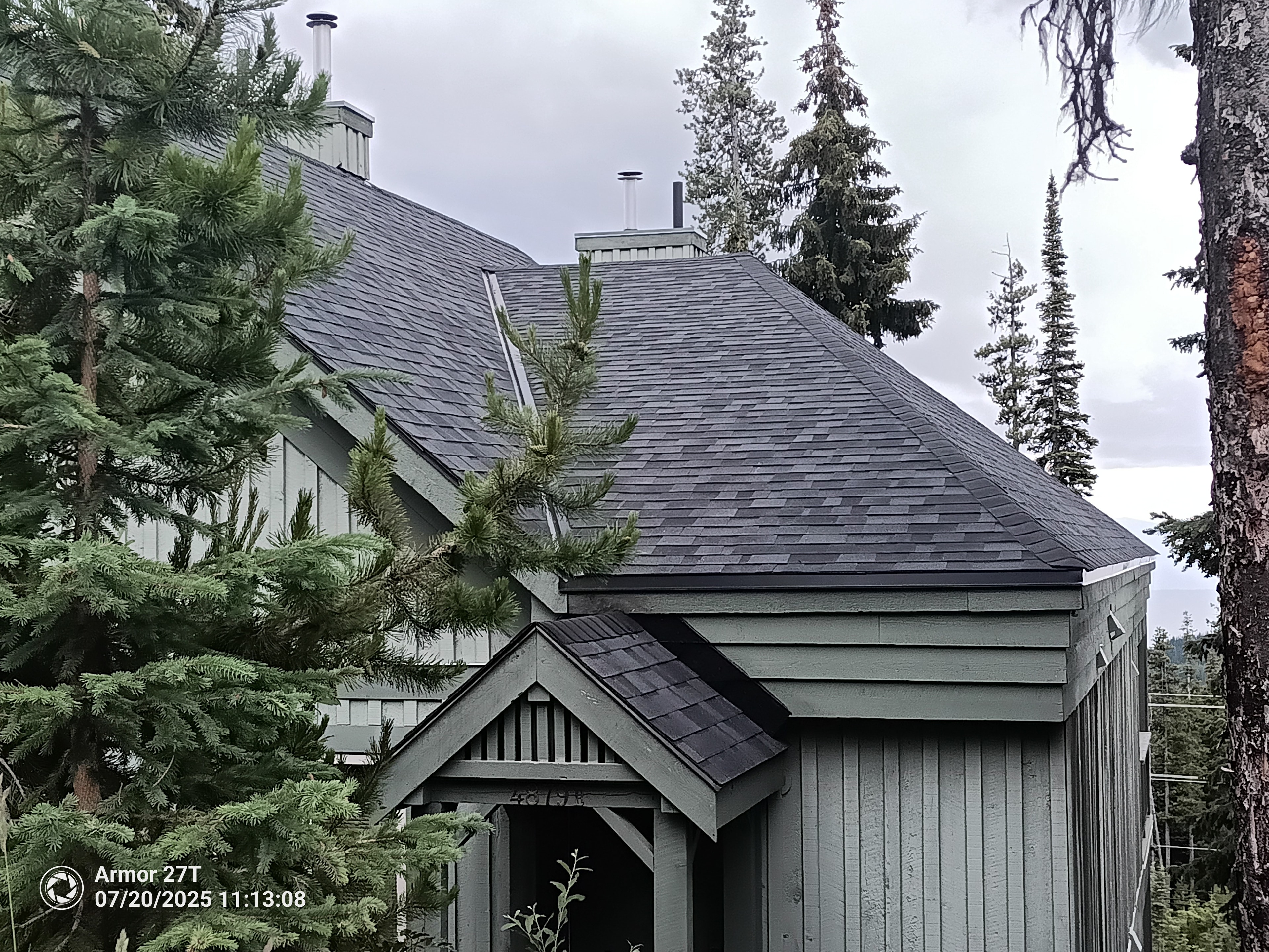 Completed dark shingle roof on chalet-style home surrounded by forest