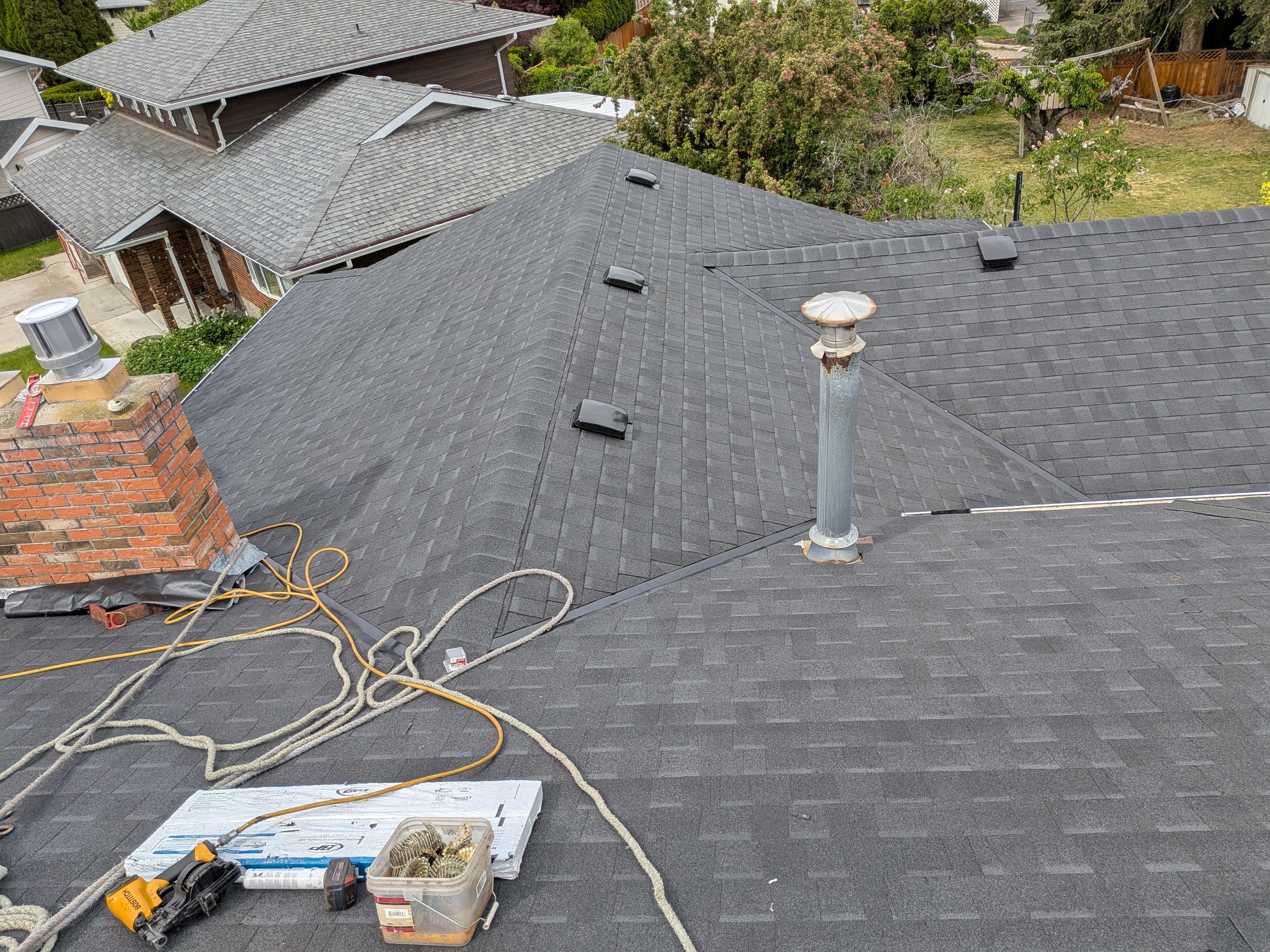 Aerial view of completed dark shingle reroof with chimney flashing and roof vents in Kelowna