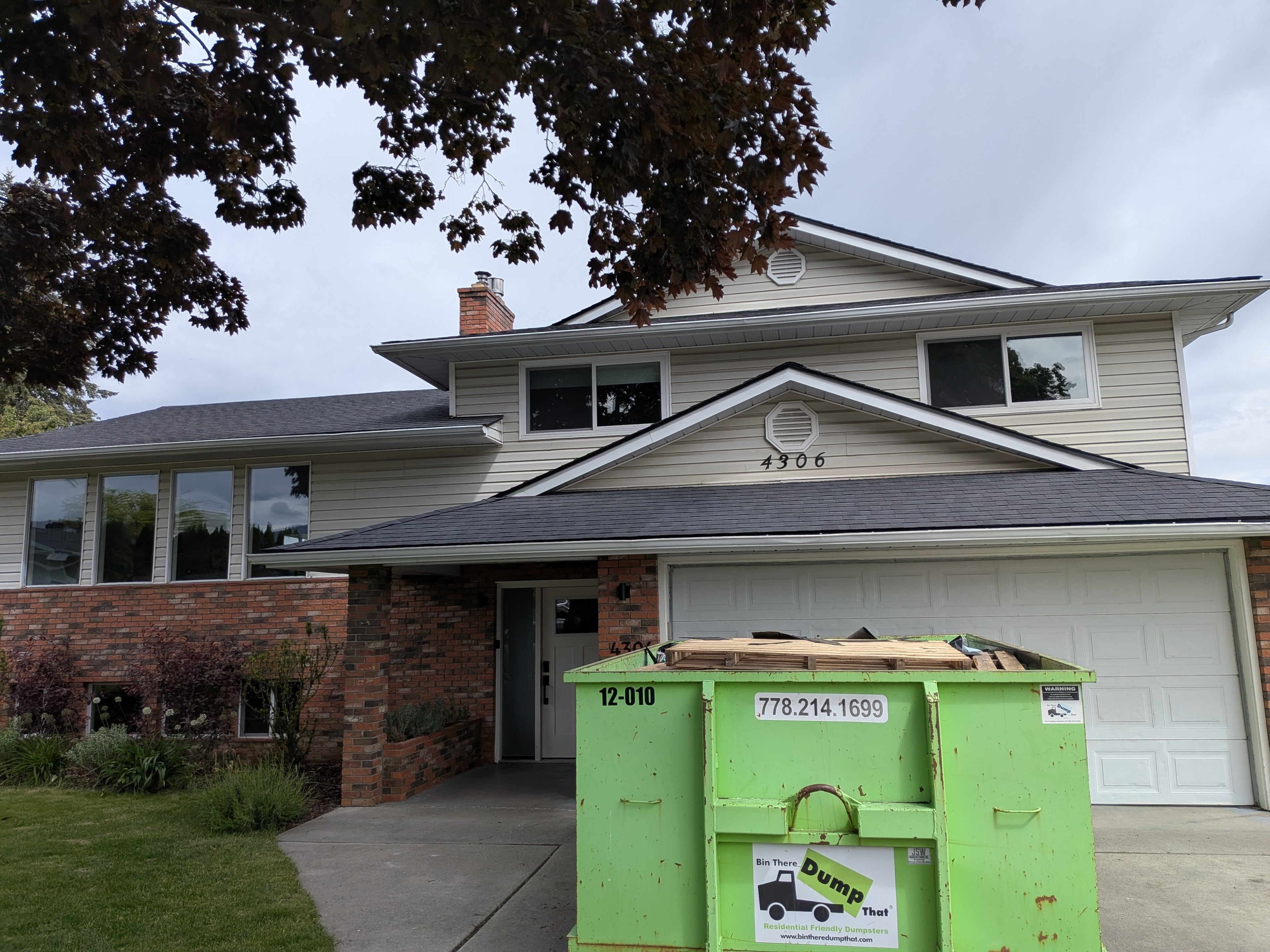Completed dark shingle reroof on two-storey brick home with dumpster in driveway