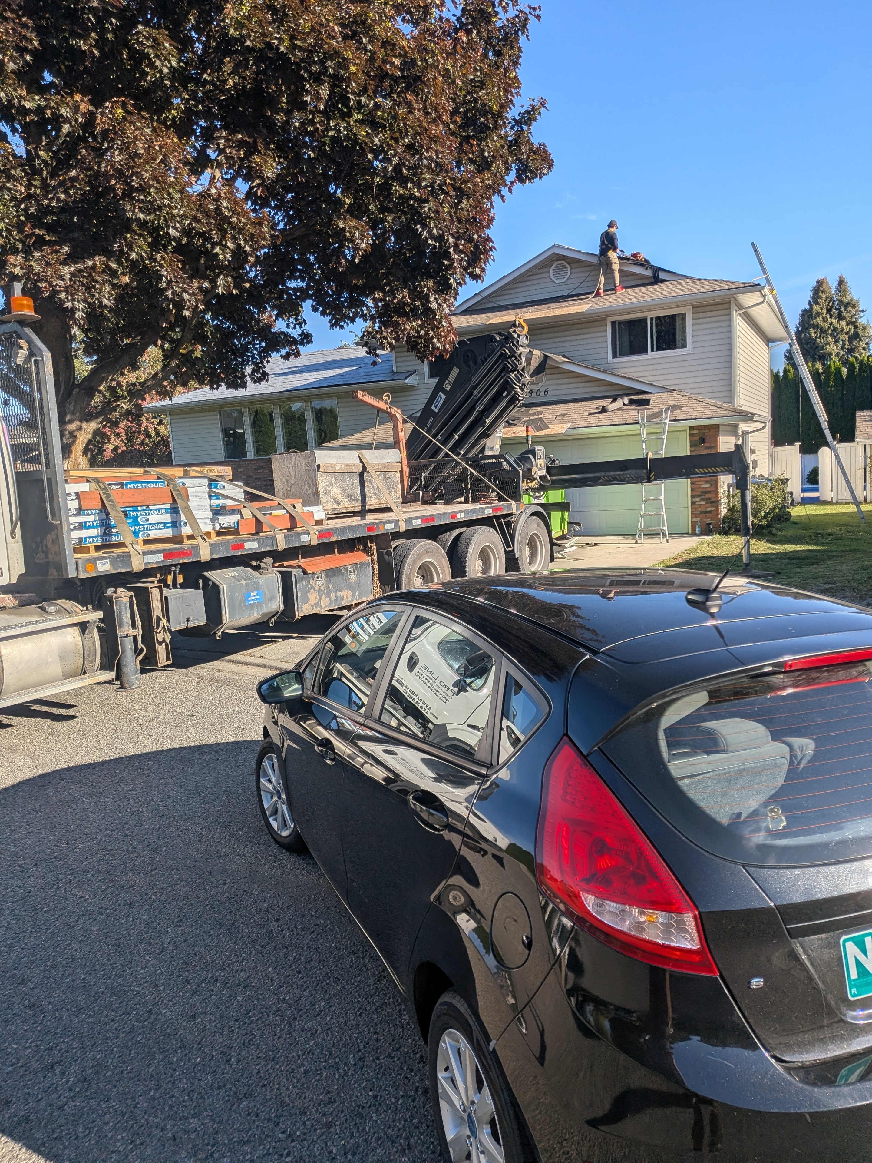 Shingle delivery truck unloading materials with roofer on roof in Kelowna
