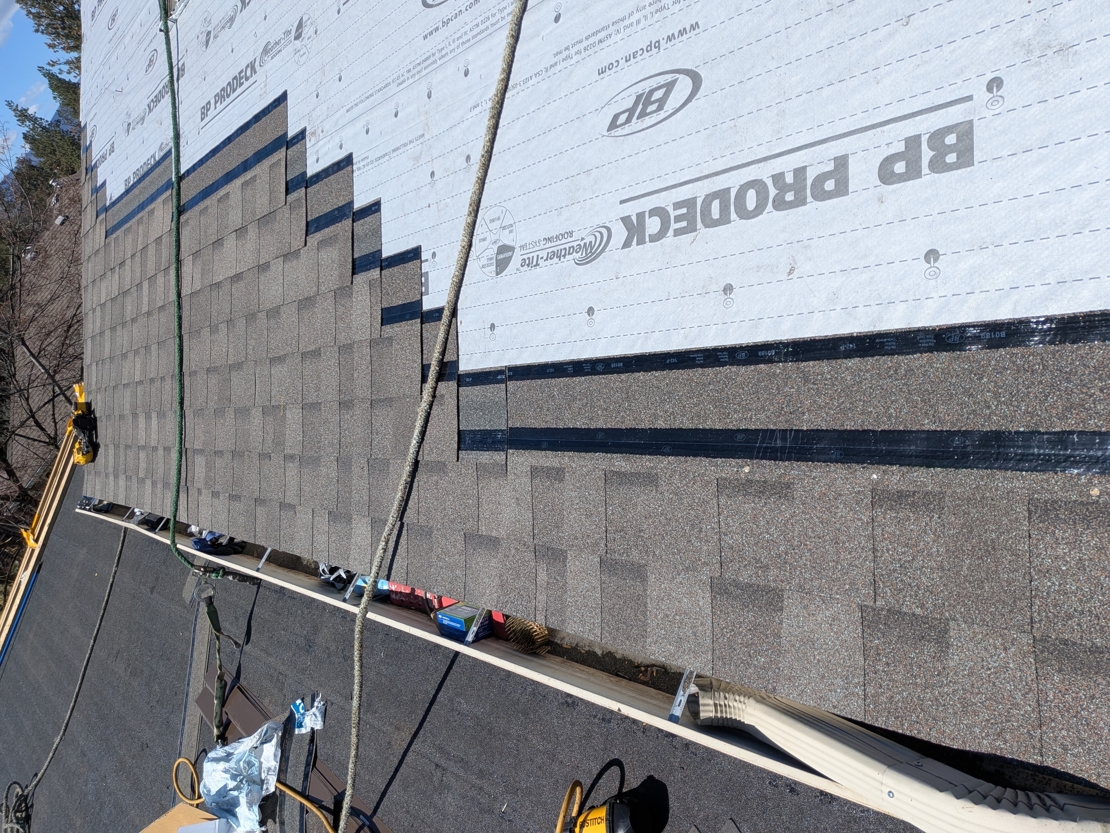 Shingle installation in progress with BP Prodeck underlayment and safety ropes on steep roof