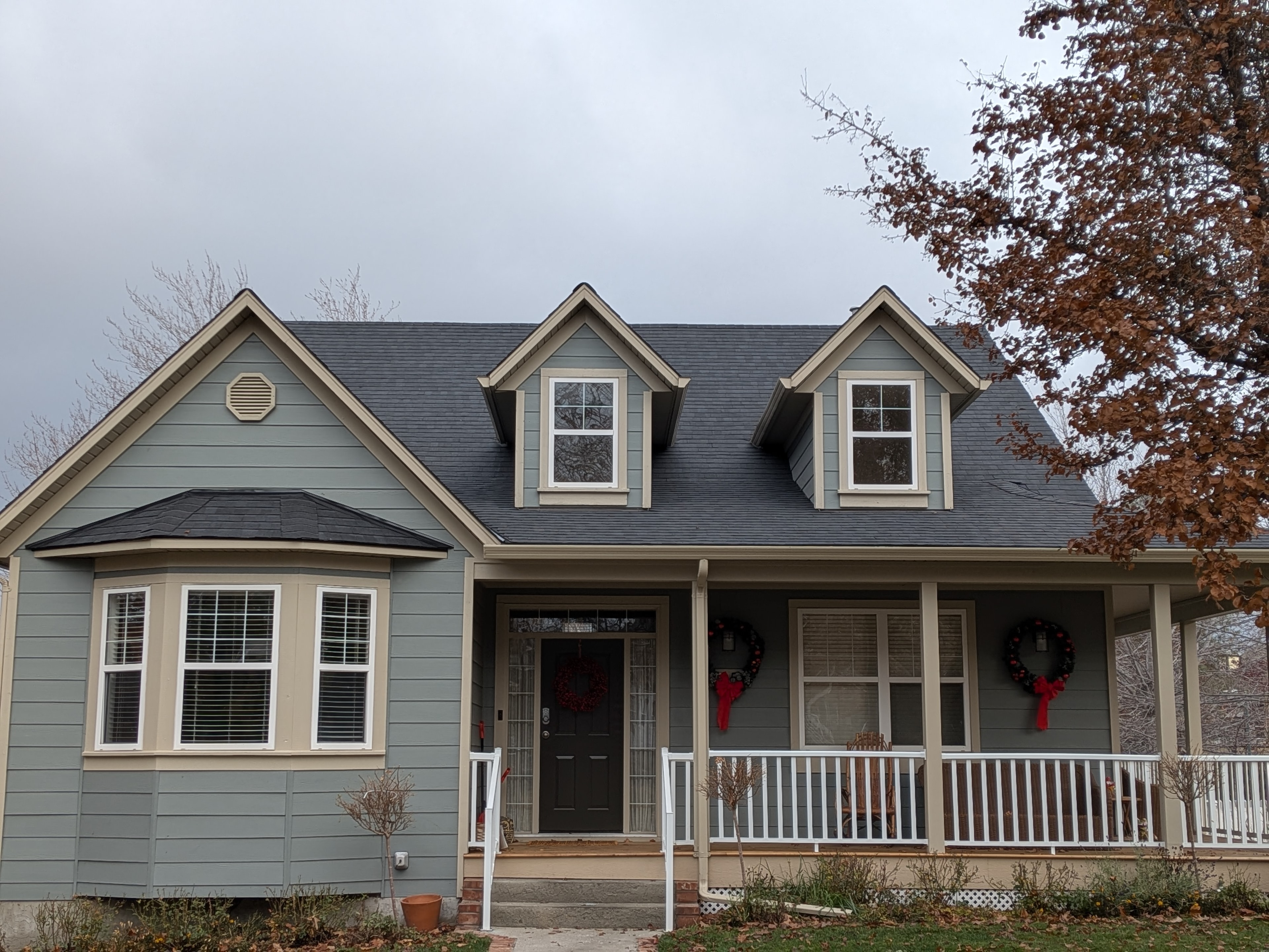 Completed dark grey shingle reroof on charming Cape Cod style home with dormers