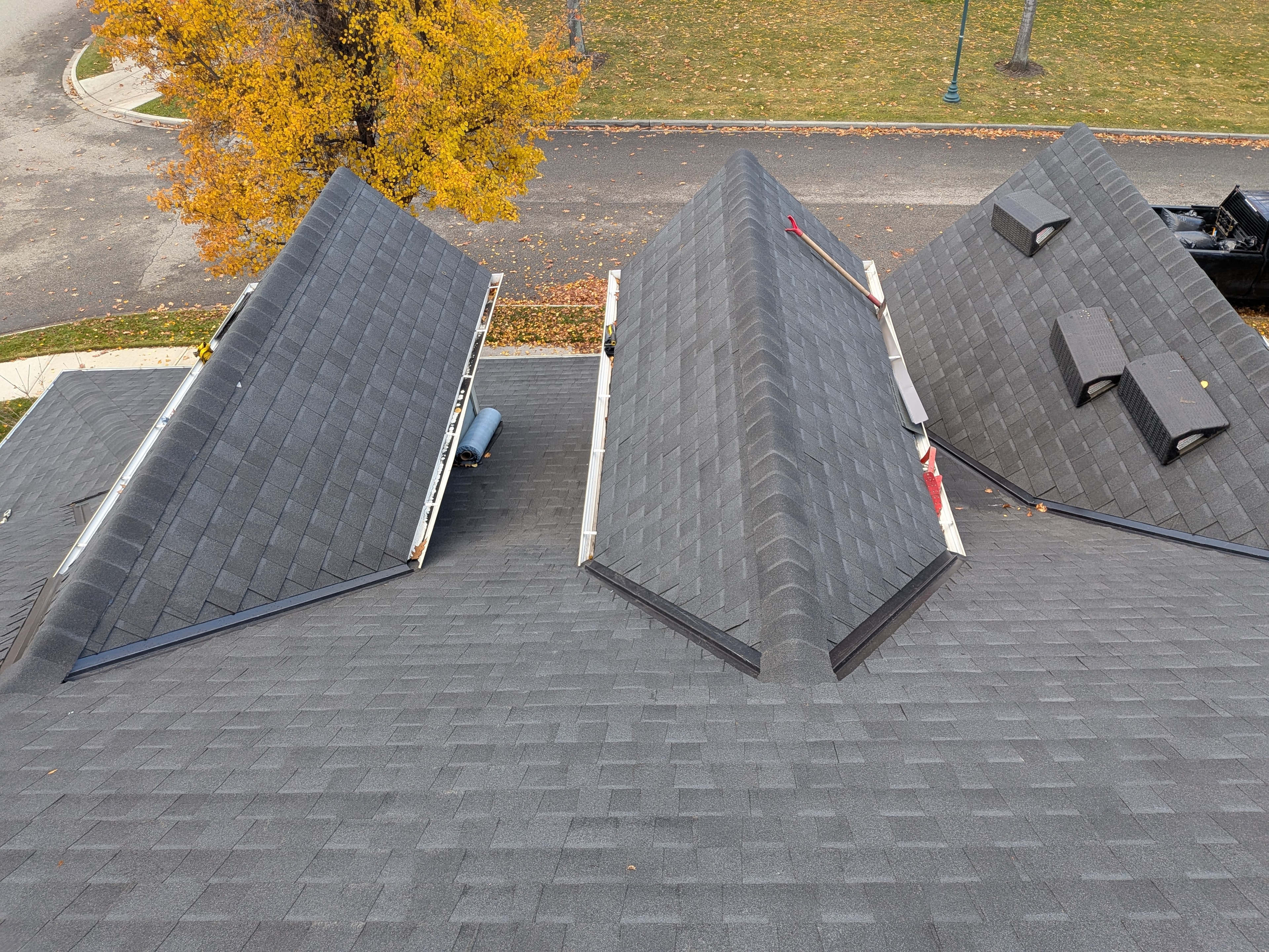 Aerial view of dark grey shingle reroof in progress with roof vents and autumn tree backdrop