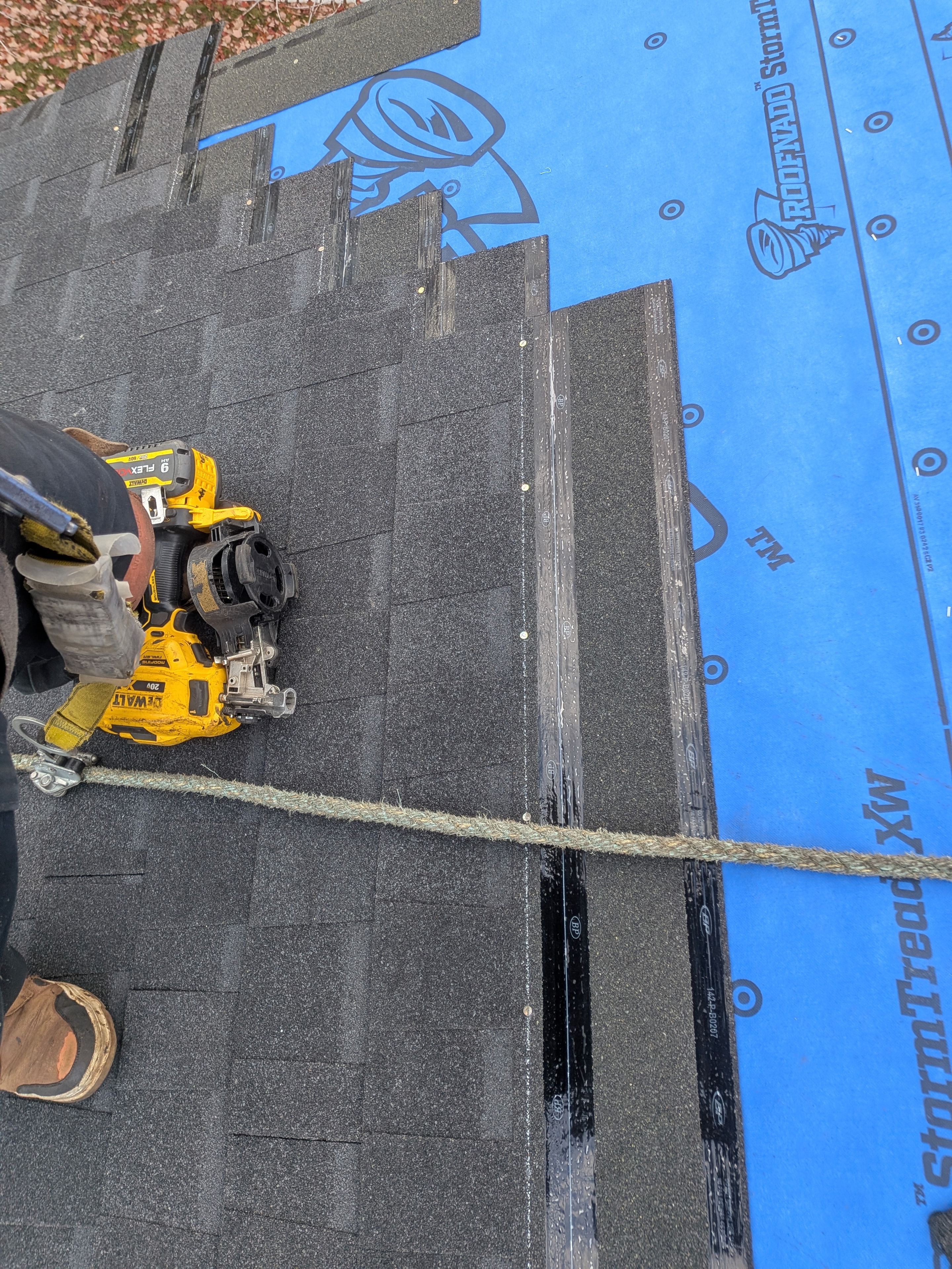 Roofer installing shingles with DeWalt nail gun alongside Roofnado StormTread blue underlayment