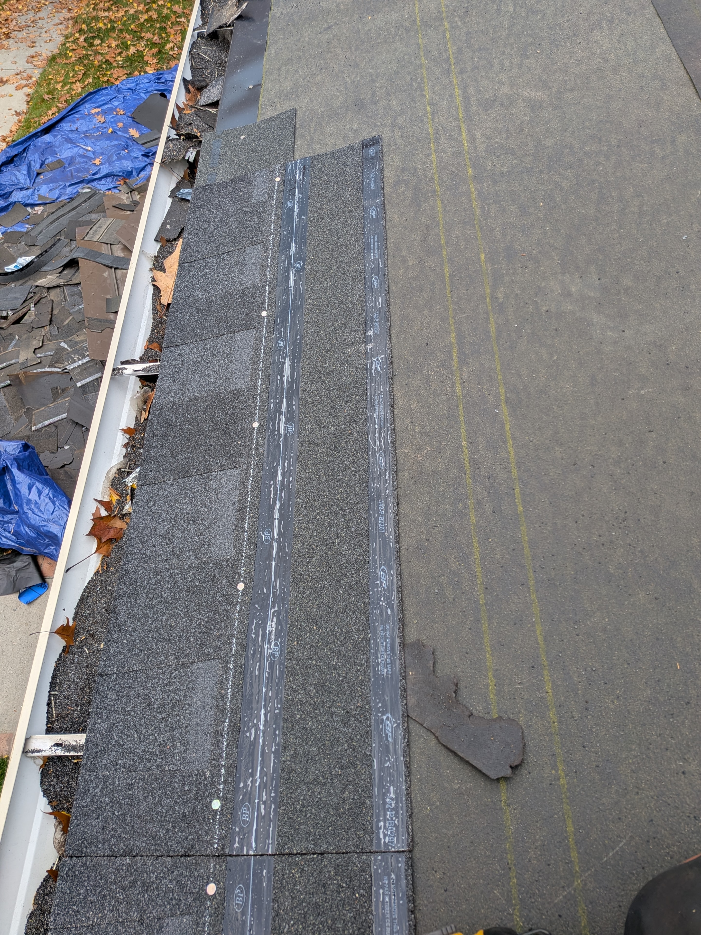 New shingles and drip edge being installed alongside torn-off old shingles on eave
