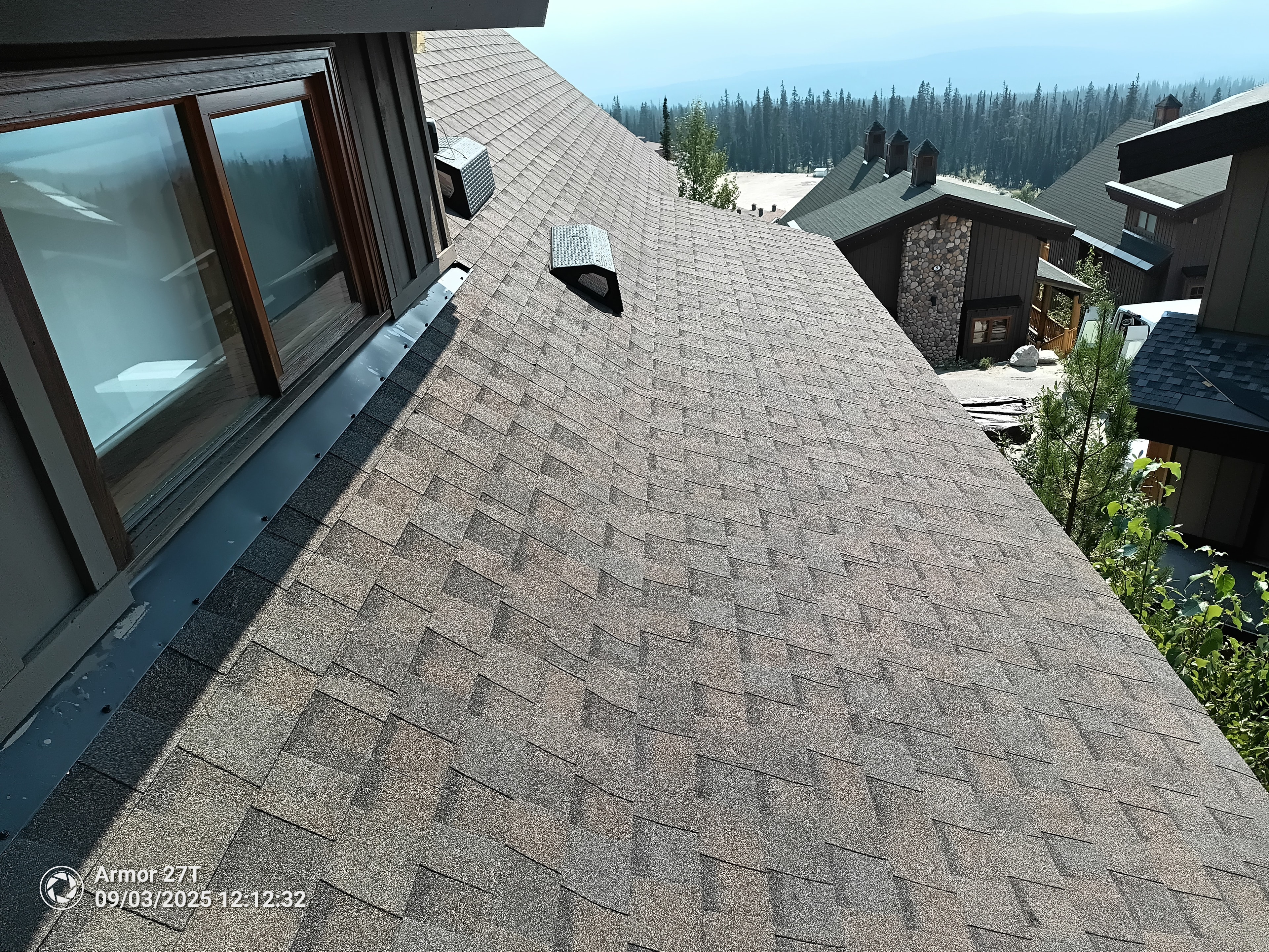 Completed tan shingle roof on chalet building at Big White with mountain and forest views