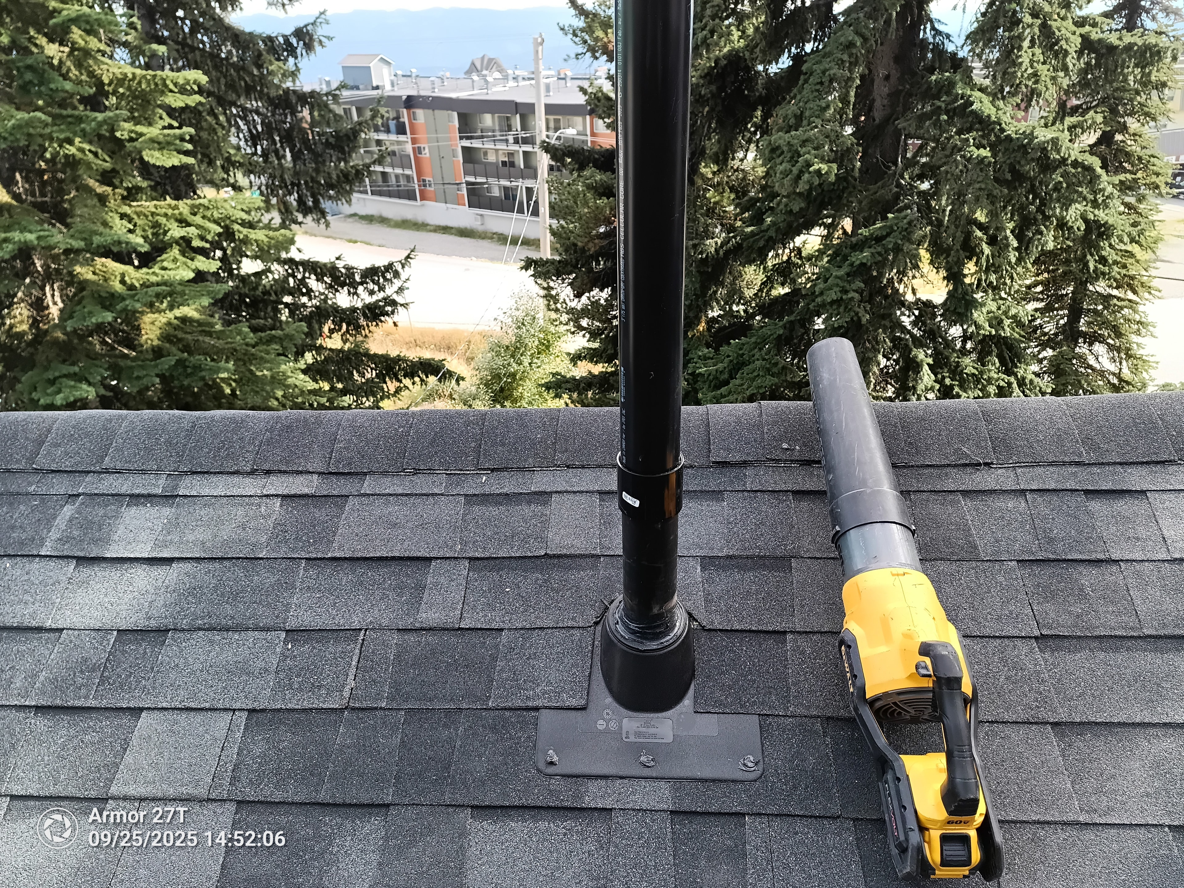 Pipe boot flashing installation on completed dark grey shingle roof with Kelowna city views