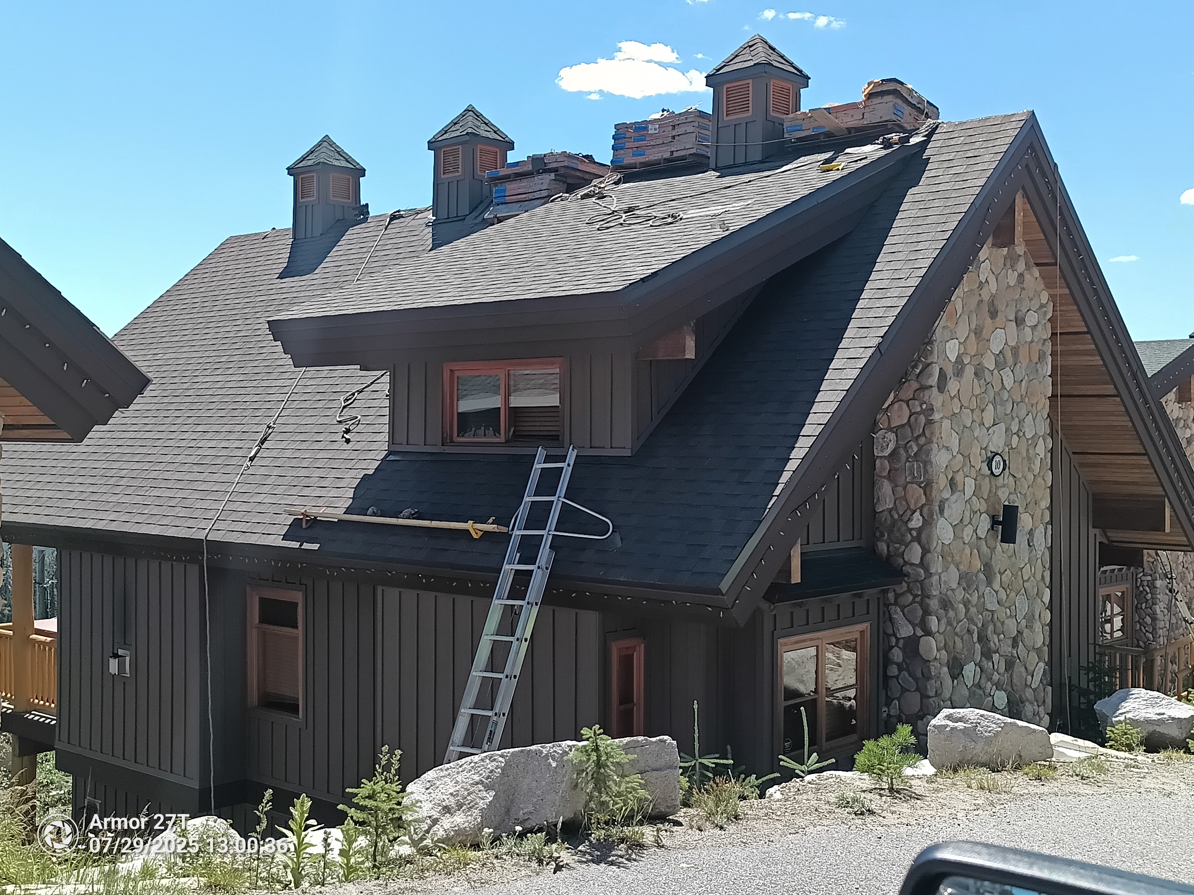 Stone and wood chalet building at Big White Ski Resort with shingle reroof in progress and ladder