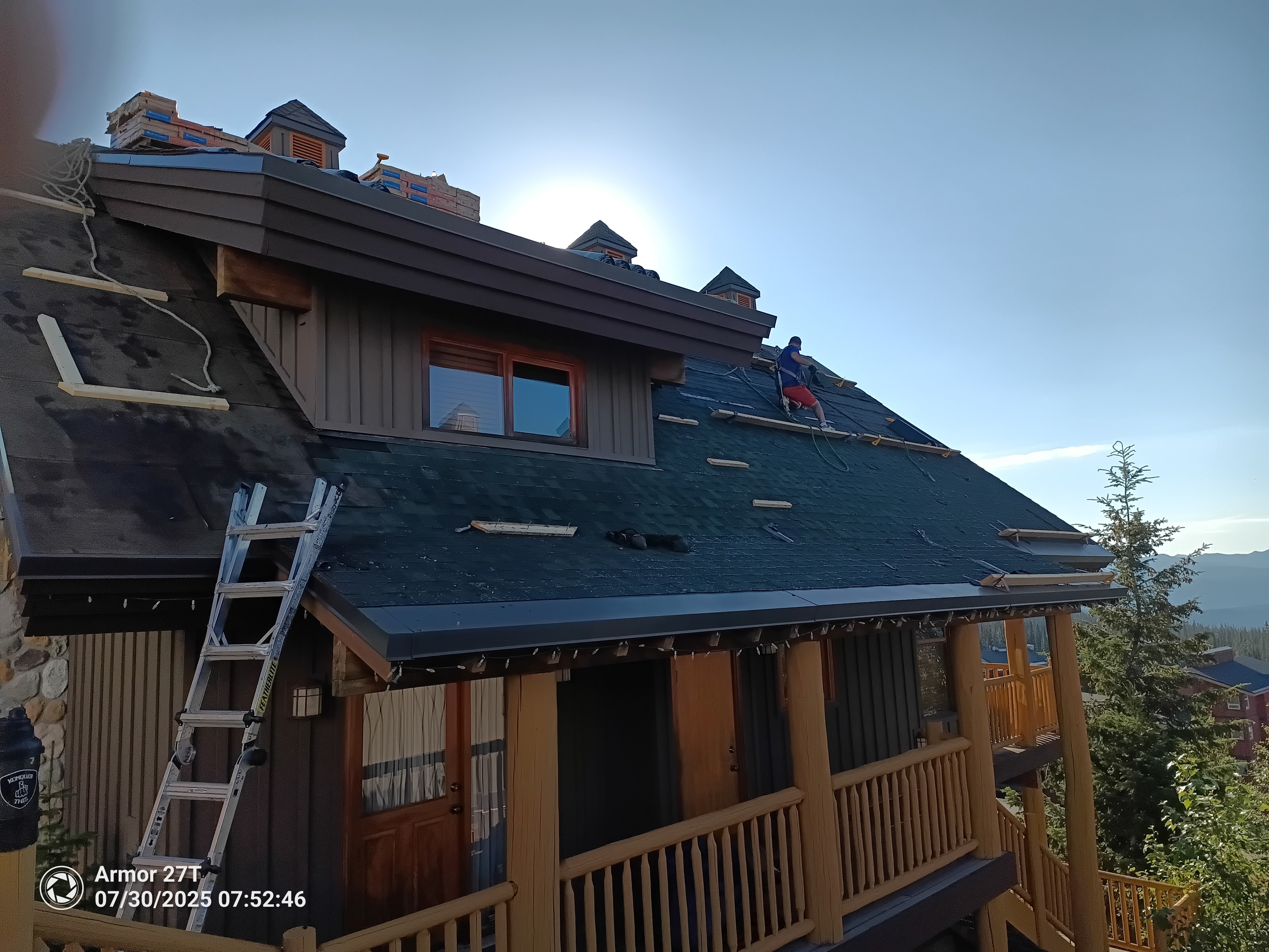 Roofer working on steep chalet roof at Big White with safety rope, mountain views and blue underlayment